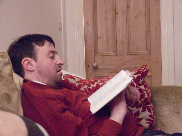 Andrew sitting on the sofa reading a bible